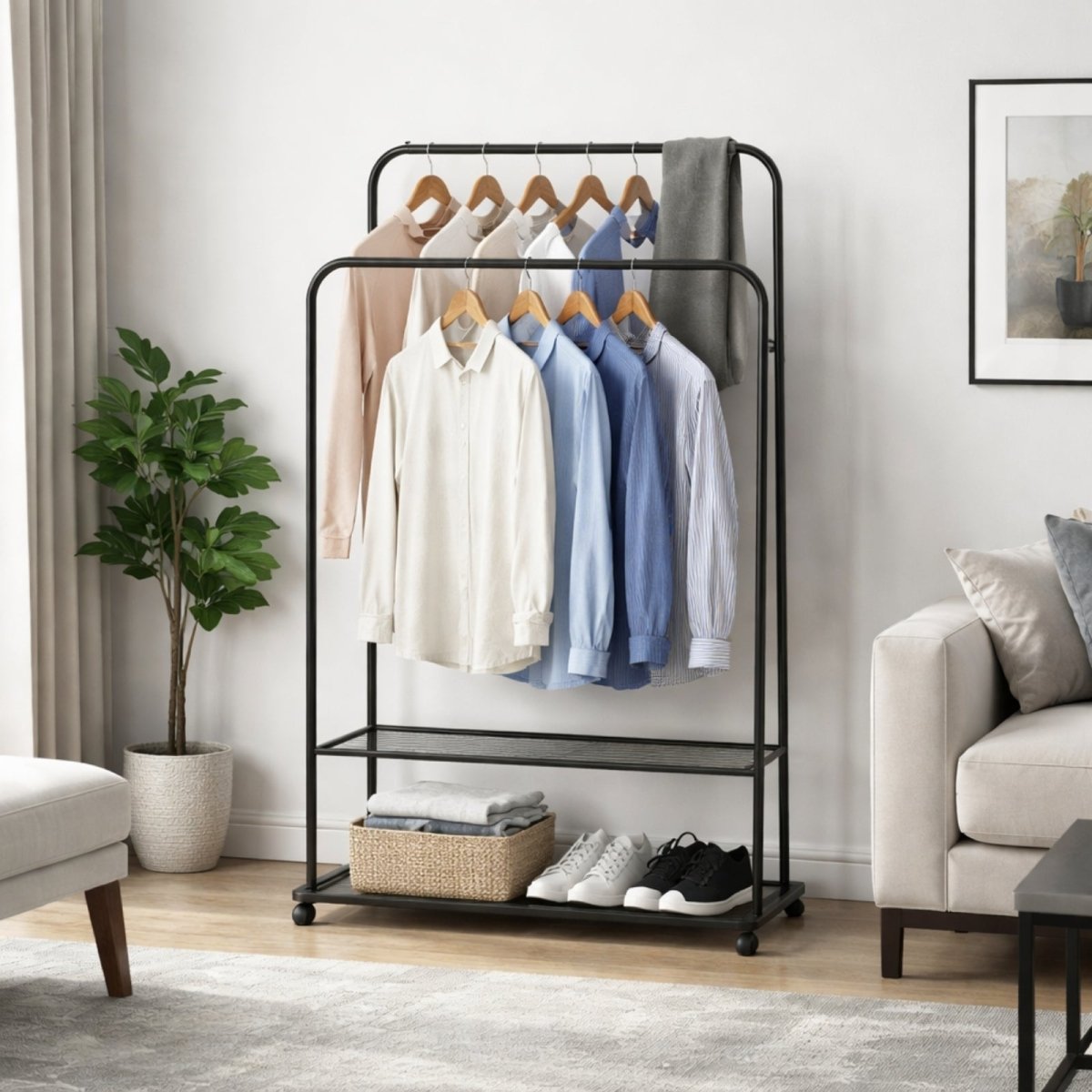 A fully styled Kouvr black metal clothes rack with shirts on two tiers, and a basket of folded clothes and sneakers on the wire mesh shelves in a modern living space.