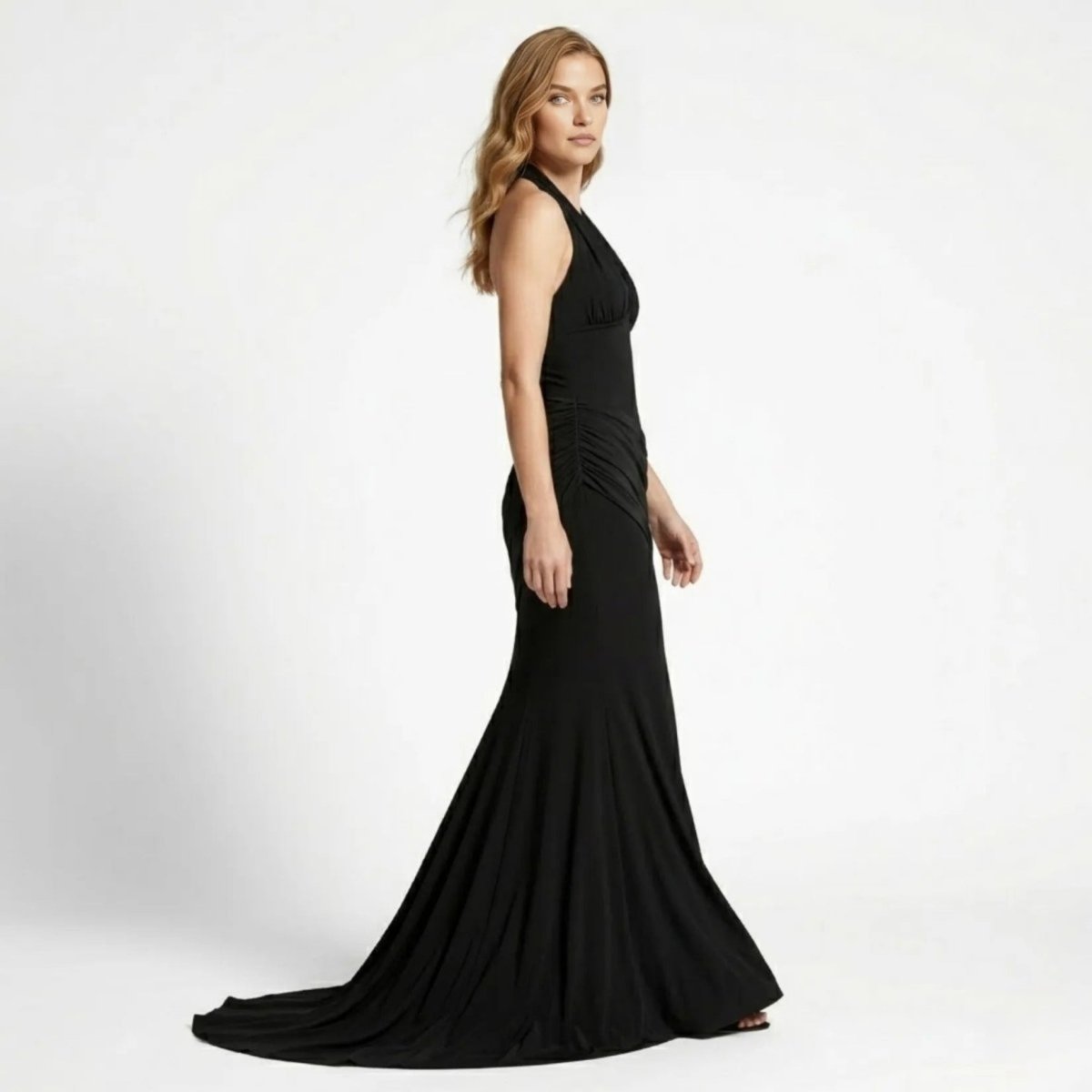 Side profile view of a glamorous black form-fitting mermaid evening gown highlighting asymmetrical draped hip details by Kouvr.