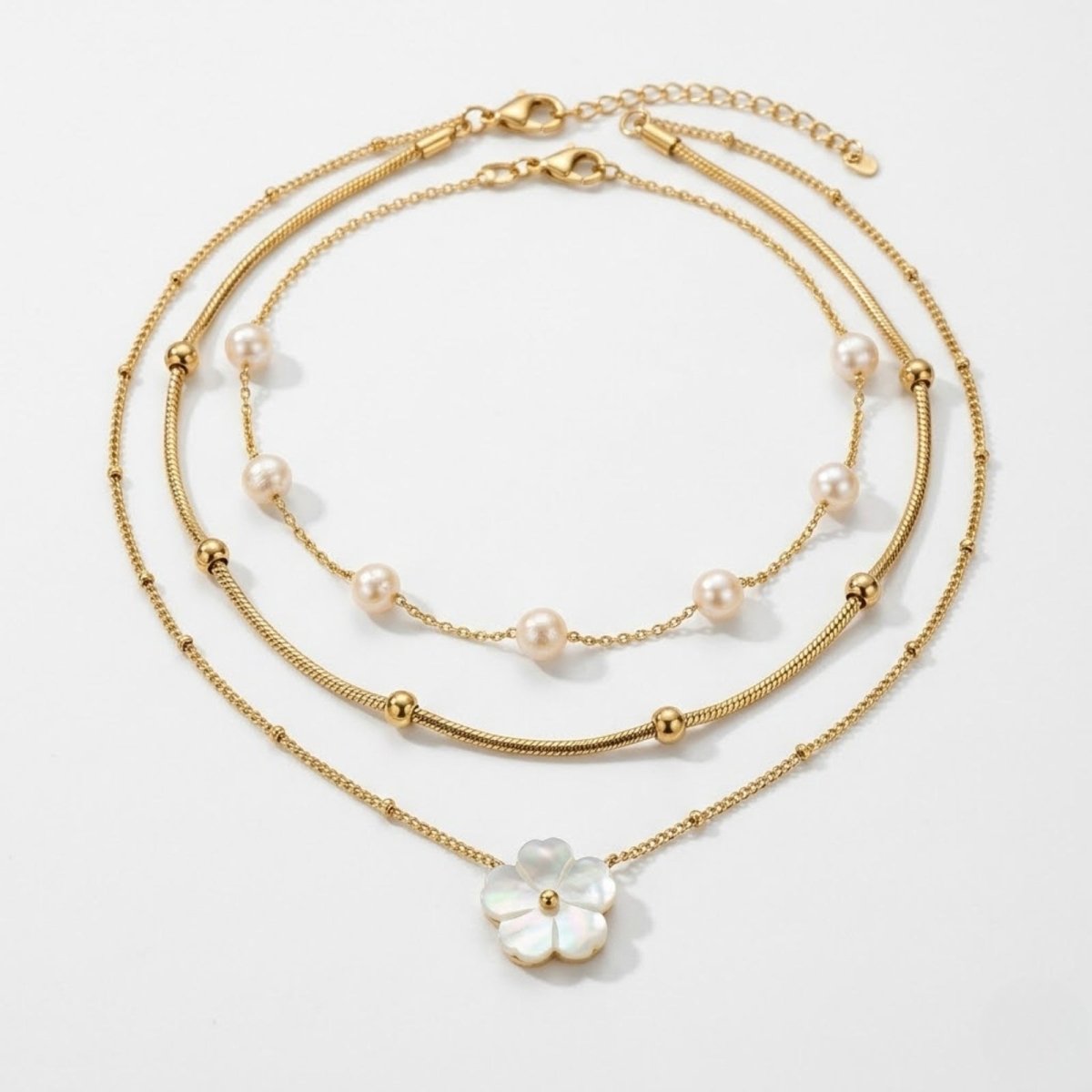 Kouvr Brisa three-piece gold layered necklace set featuring a pearl strand, a gold bead snake chain, and a mother-of-pearl flower pendant on a white background.
