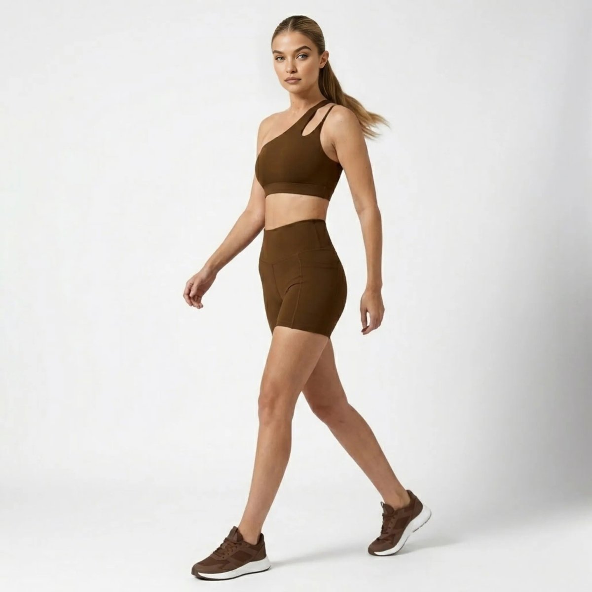 Profile view of woman walking in Kouvr brown asymmetrical matching gym outfit with side pockets