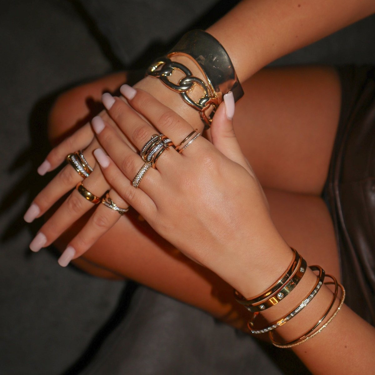 Kouvr hand wearing multiple gold bracelets and rings on a dark background