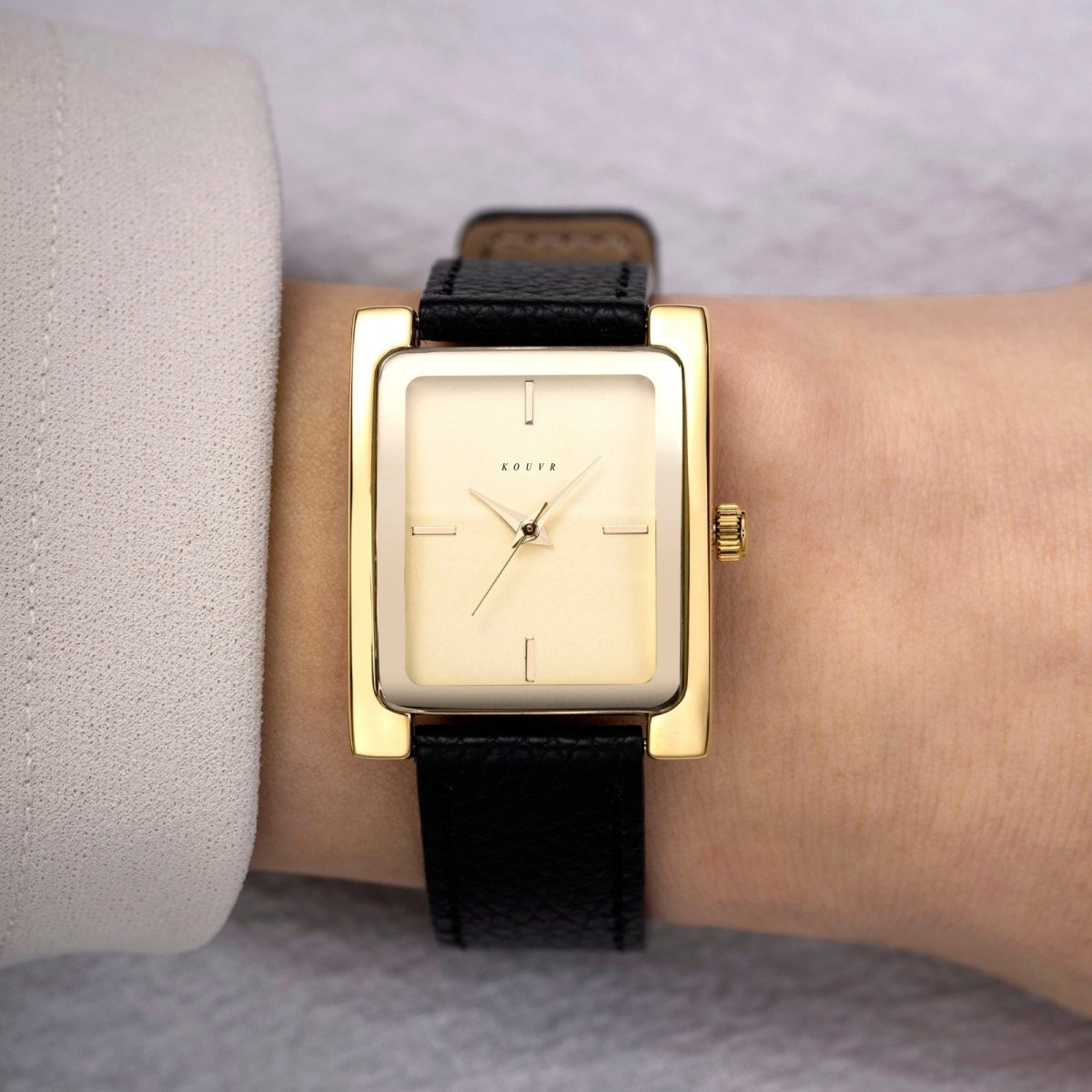Gold Kouvr square watch with black strap on a wrist against a neutral background
