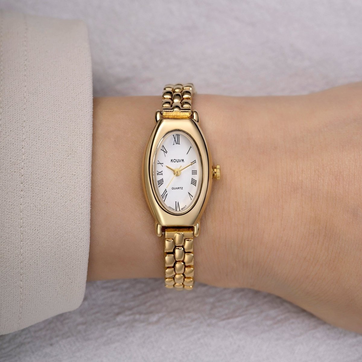 Gold wristwatch on a person's wrist with a neutral background