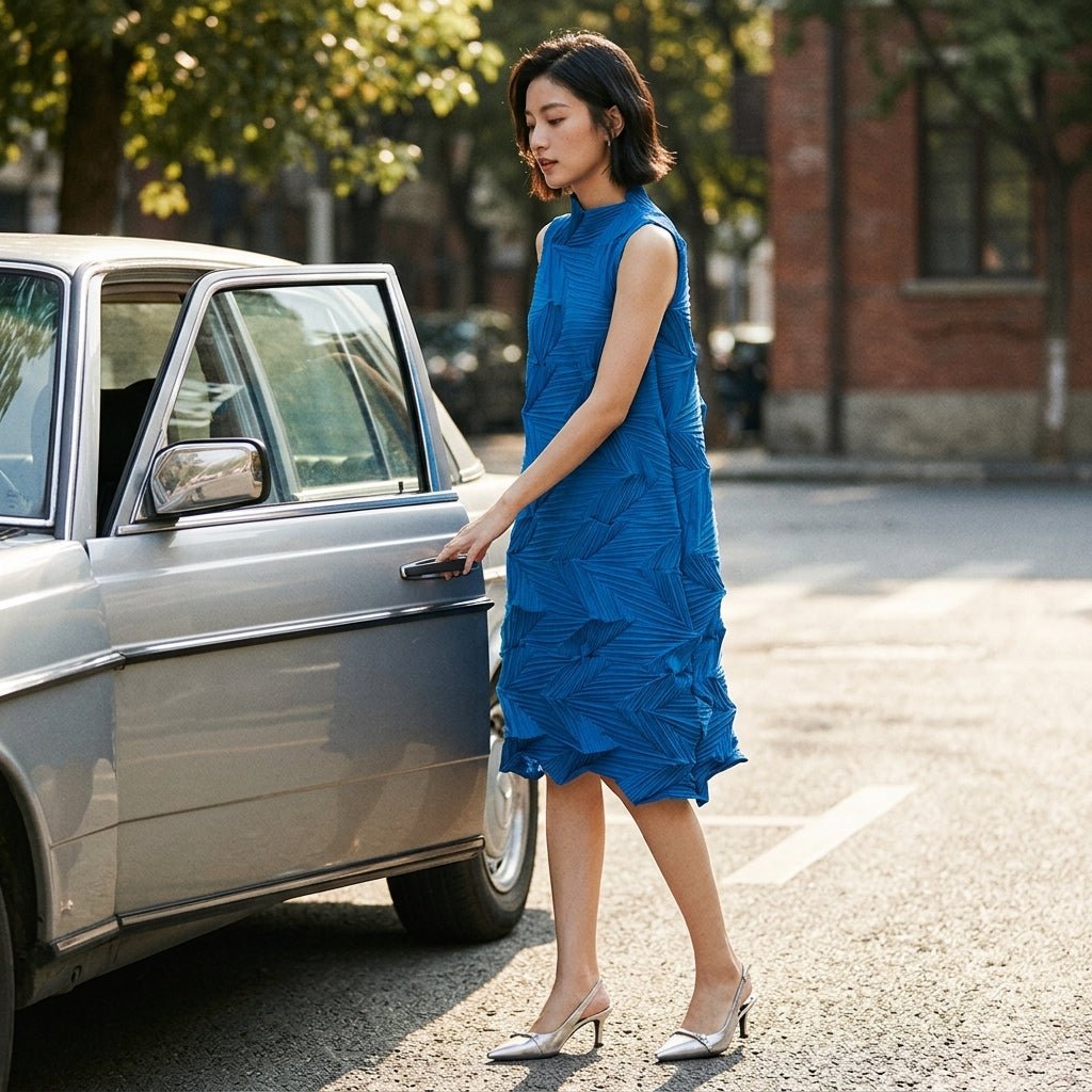 Asian female model stepping out of a vintage silver car wearing the Kouvr blue pleated midi dress and metallic heels.