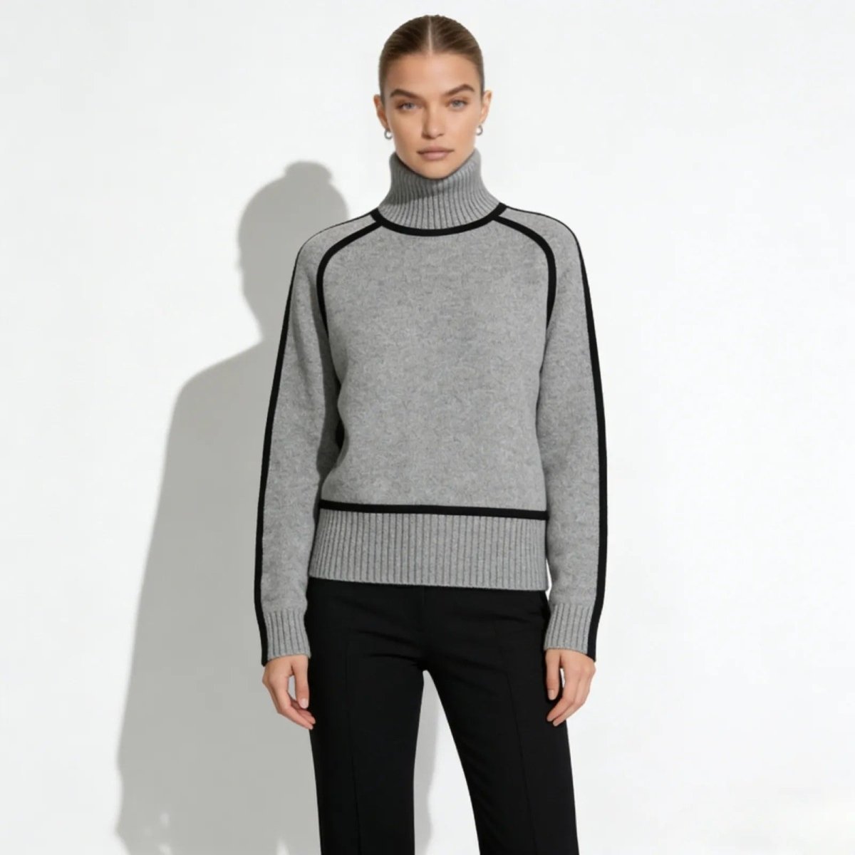 Model wearing Kouvr's gray cashmere turtleneck sweater with black piping detail, front view.
