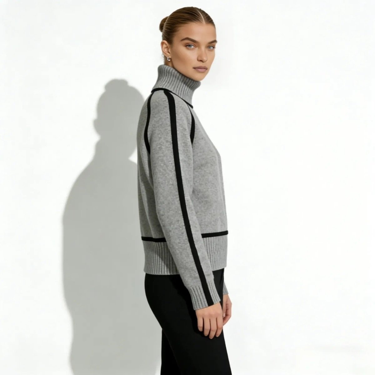 Side profile of a woman in a gray high-neck sweater featuring black stripes along the raglan sleeves.