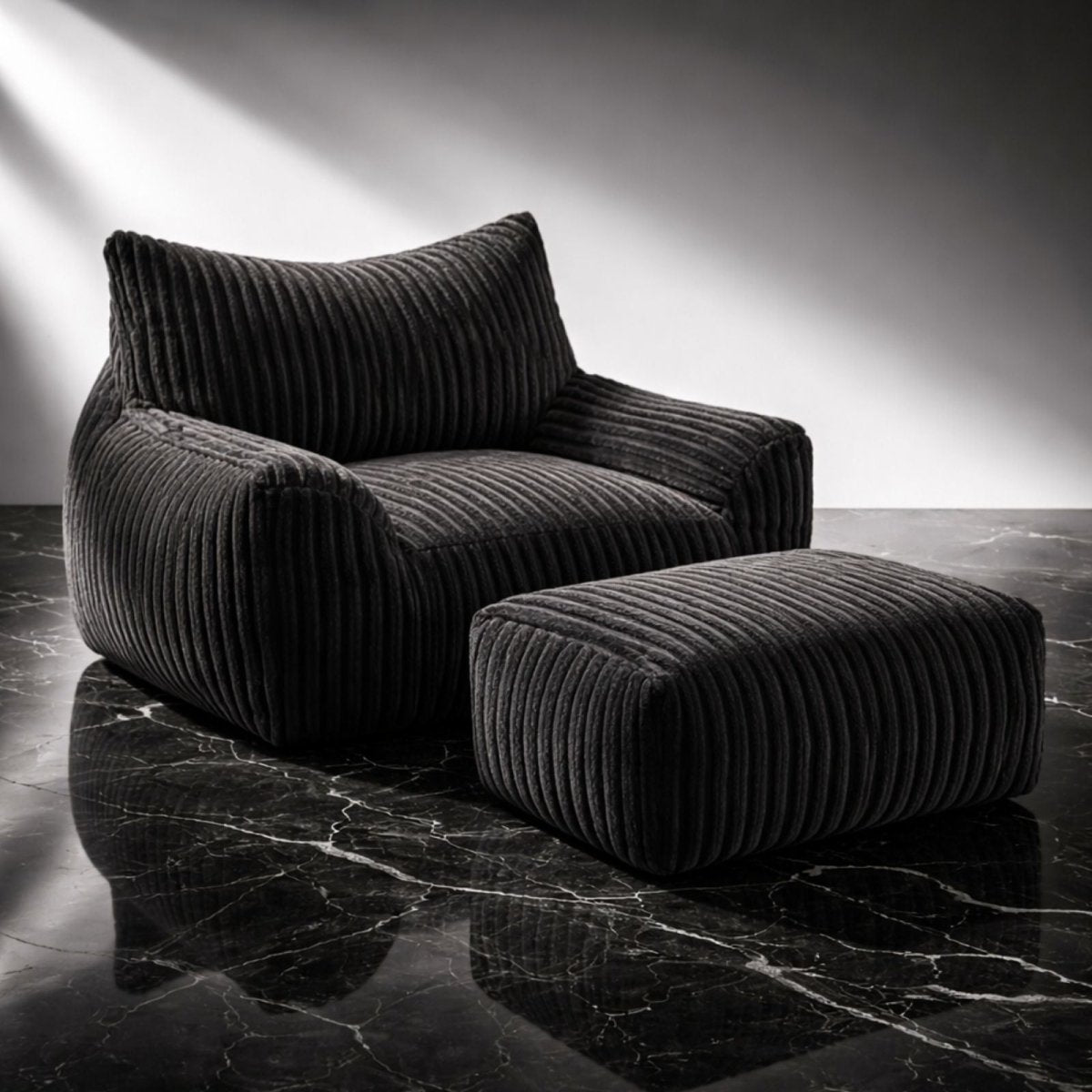 The Kouvr oversized corduroy lounge chair and ottoman set in, shown in a studio with dramatic lighting highlighting its deep ribbed texture.