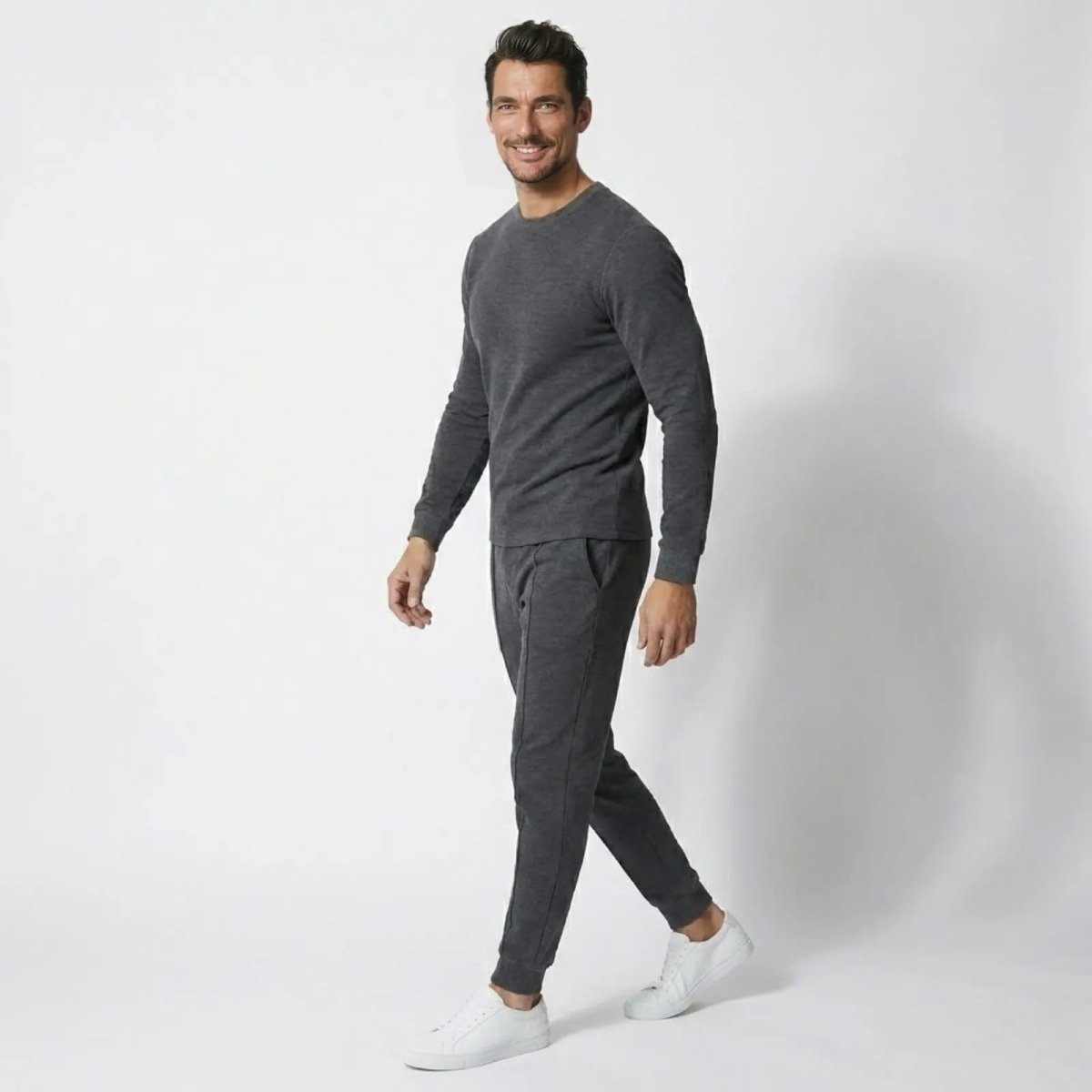 Side profile view of a man walking in the charcoal grey Kouvr Crue Knit Lounge Set, showcasing its slim fit and white sneakers.