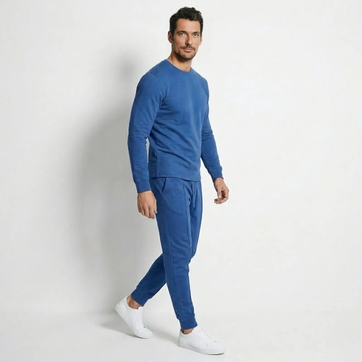 Side profile view of a man in a blue cotton tapered jogger and sweatshirt tracksuit, showing the tailored fit and pintuck seam detail.