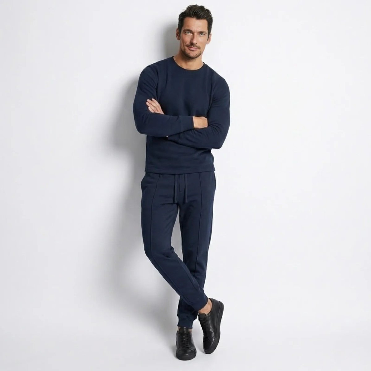 Male model wearing the Kouvr Crue lounge set in navy, leaning against a white wall with arms crossed to show the tailored fit.
