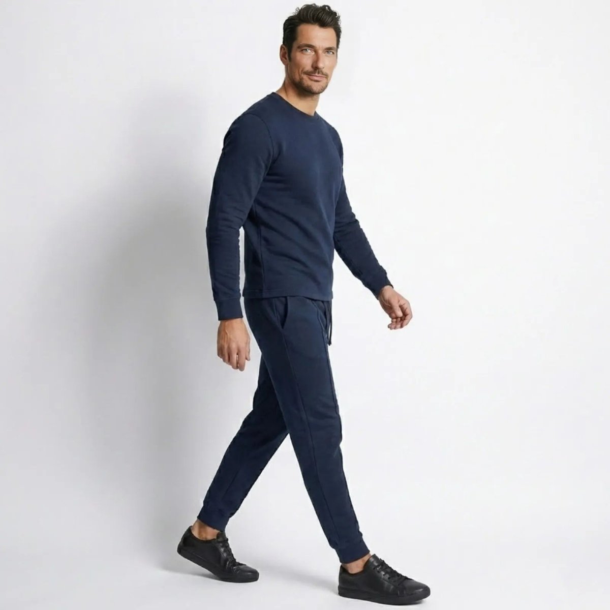 Side profile of a model walking in the Kouvr Crue navy tracksuit, showcasing the garment's drape and slim silhouette.
