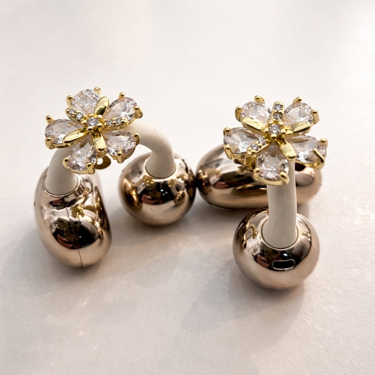 A pair of Kouvr crystal flower wireless Hollis earrings with a gold finish and brilliant-cut crystals sitting on a white surface.
