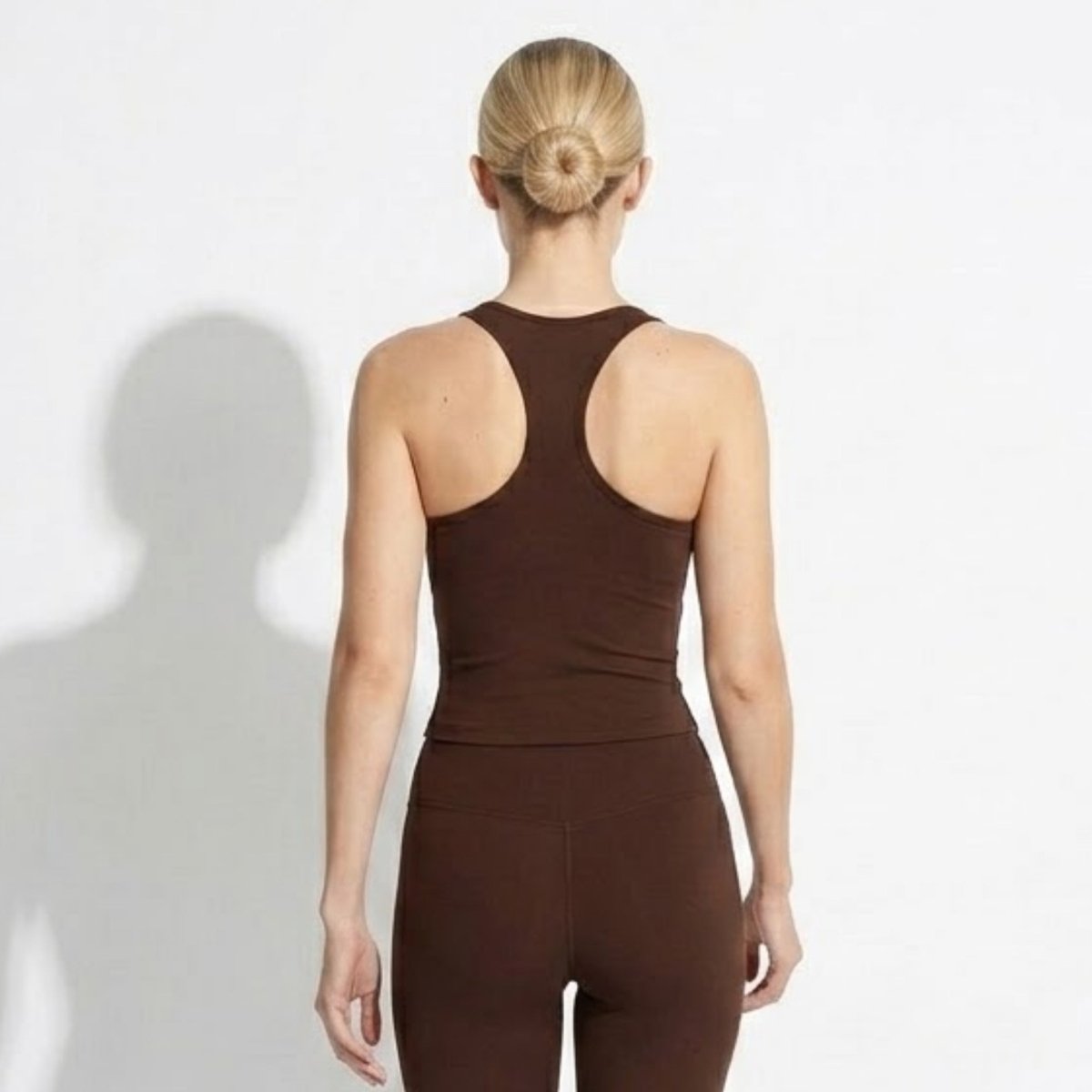 Back view of woman wearing Kouvr dark brown activewear tank top highlighting racerback strap design