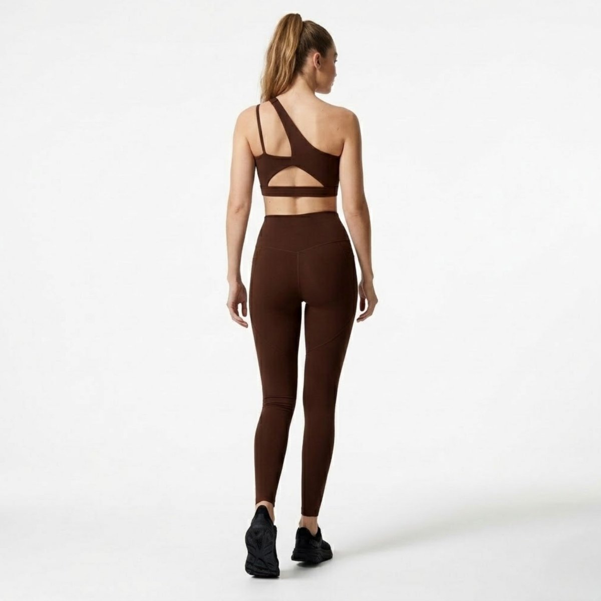 Back view showcasing the open back strap detail of the sports bra and the glute contouring seams on the high waisted brown leggings.