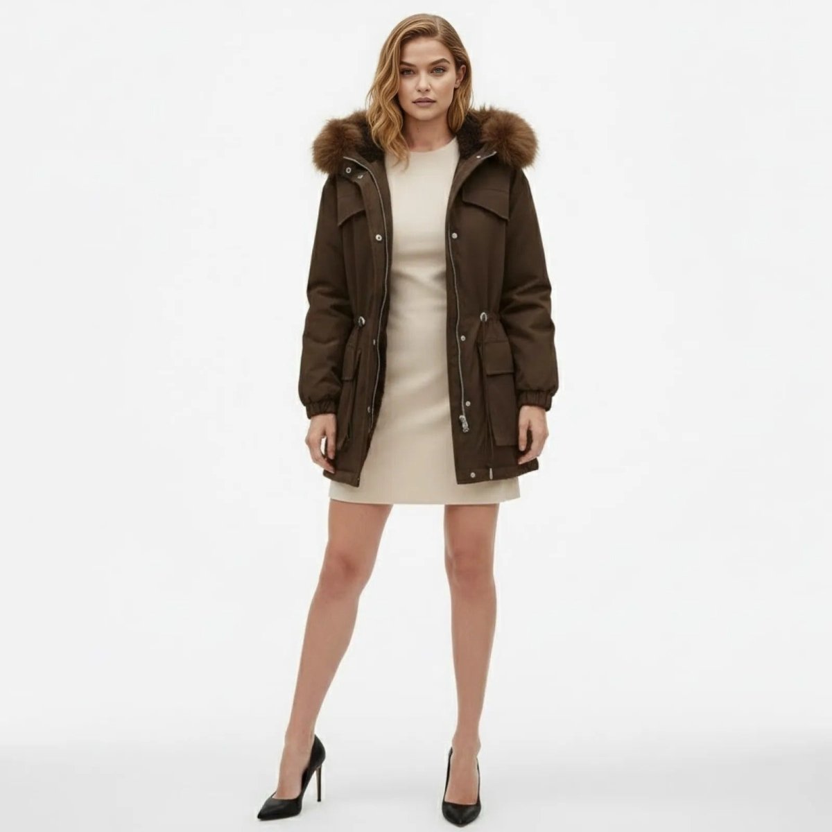 Model facing front wearing the Kouvr Debra brown winter parka with a faux fur hood, paired with a cream dress and black heels.