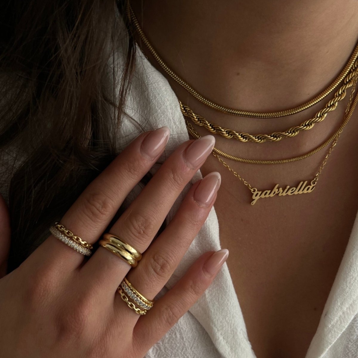 Close-up of a person wearing gold kouvr jewelry including a necklace, rings, and bracelets.