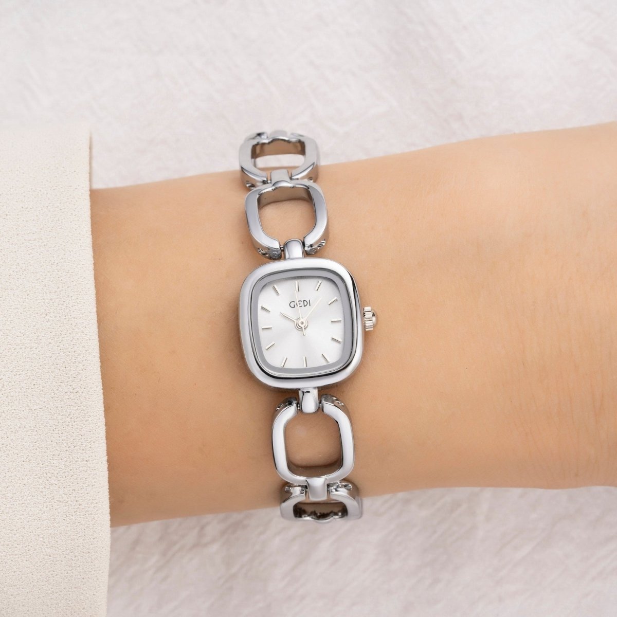 Silver kouvr watch with chain-like bracelet on a wrist against a light background