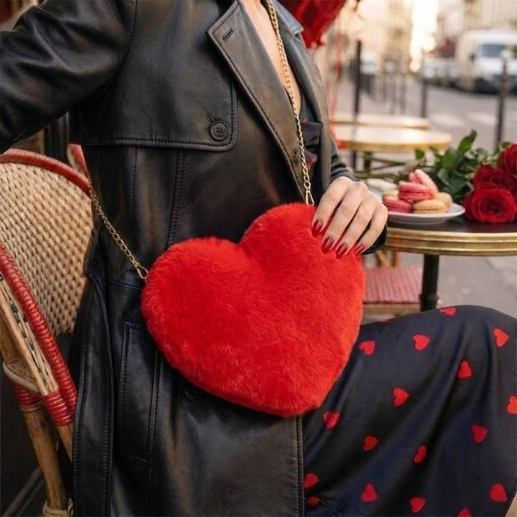 Woman in a black leather coat and heart-print dress sitting at a Parisian cafe, wearing the Kouvr Fashion Amour red faux fur heart shaped crossbody bag.