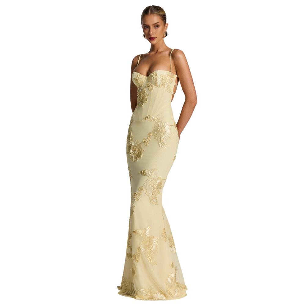 A model viewed from the back wearing the Kouvr Fashion Aphaea Gown, a backless yellow mermaid dress with 3D floral embroidery and an adjustable lace-up corset detail