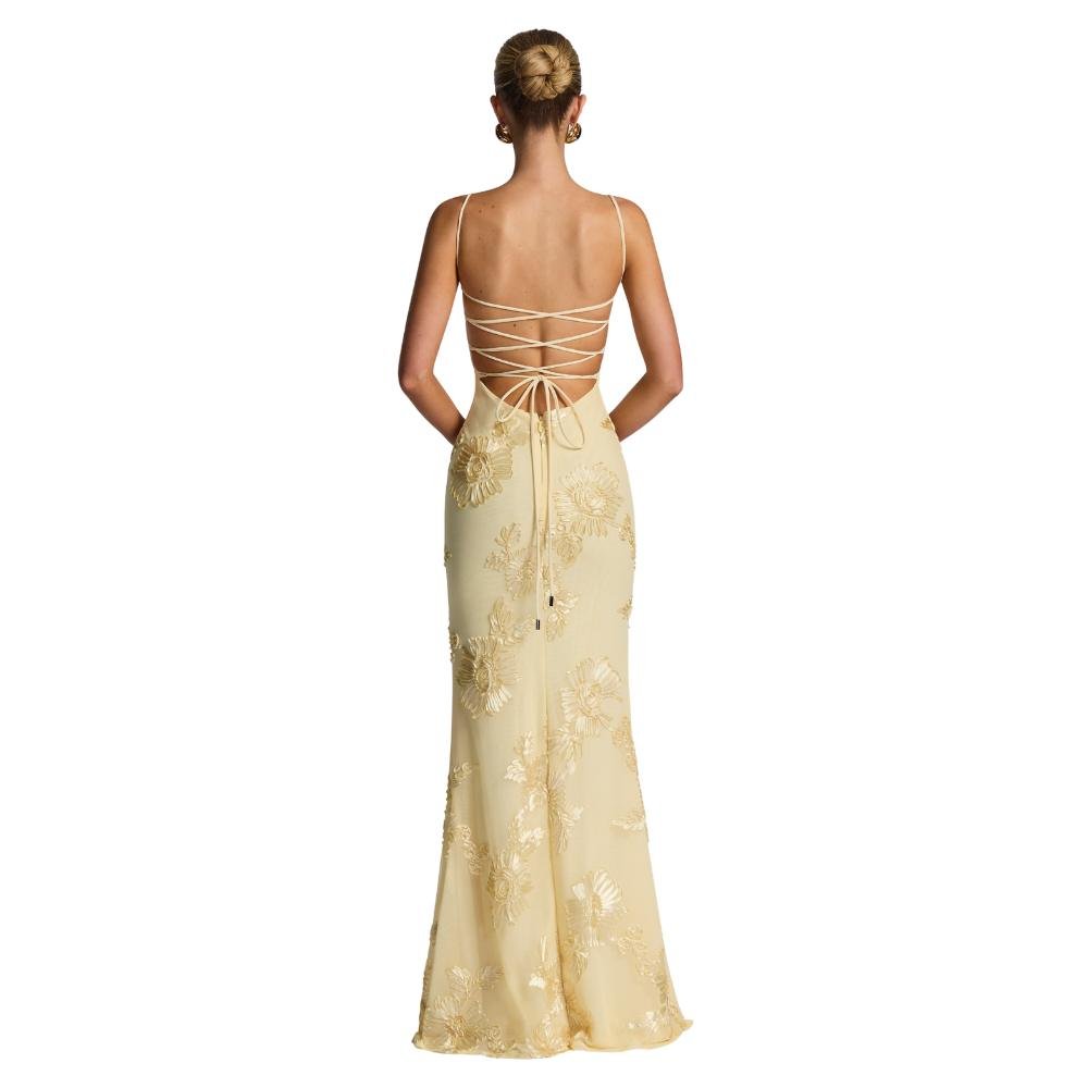 A model viewed from the back wearing the Kouvr Fashion Aphaea Gown, a backless yellow mermaid dress with 3D floral embroidery and an adjustable lace-up corset detail