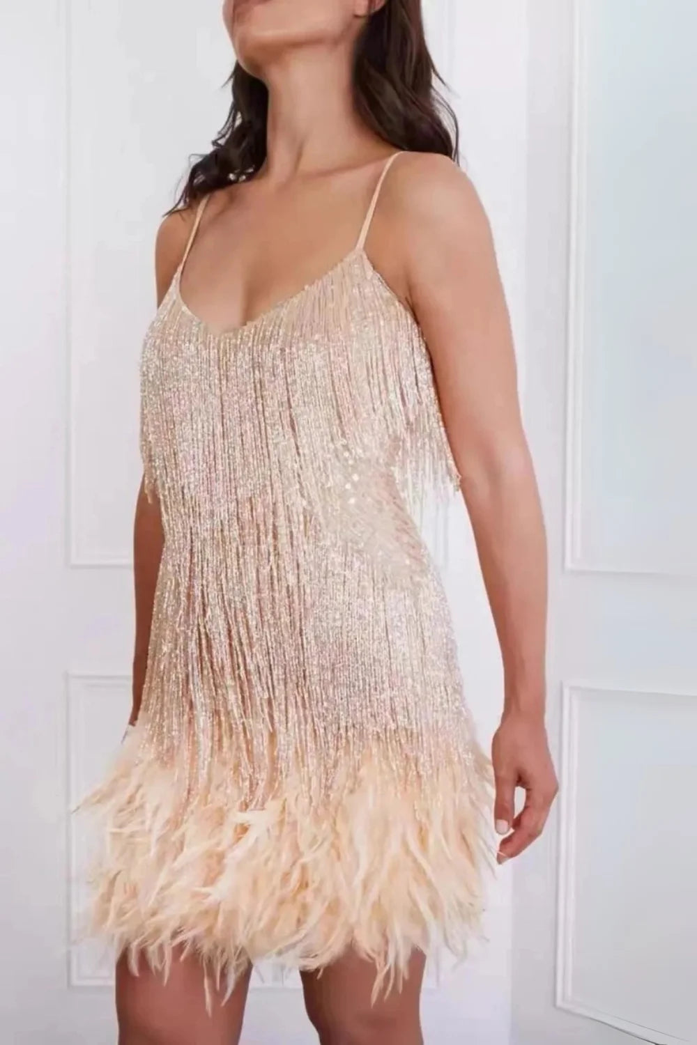 Model from the back wearing the Kouvr Fashion apricot mini dress with spaghetti straps, sequin fringe, and a feather hem