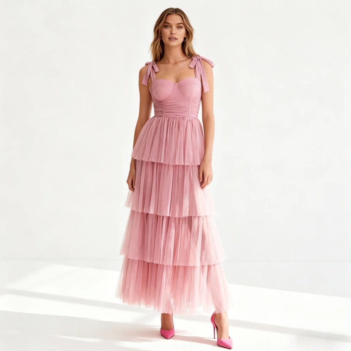 Woman wearing a pink Kouvr tiered dress with bow straps on a white background