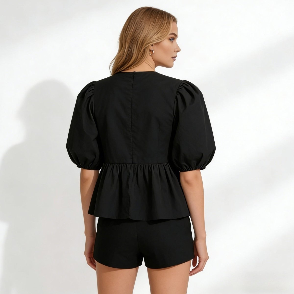Back view of the Kouvr Fashion black peplum top showing the zipper and full puff sleeve silhouette.
