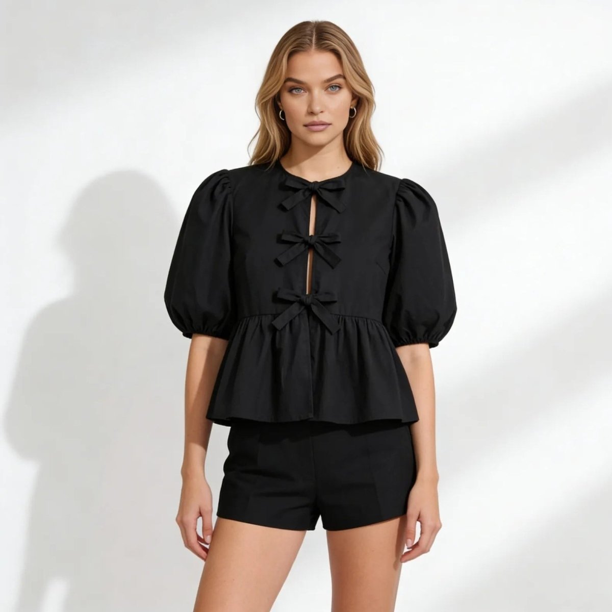 Model wearing the Kouvr Fashion black bow peplum top with puff sleeves and matching shorts, front view.