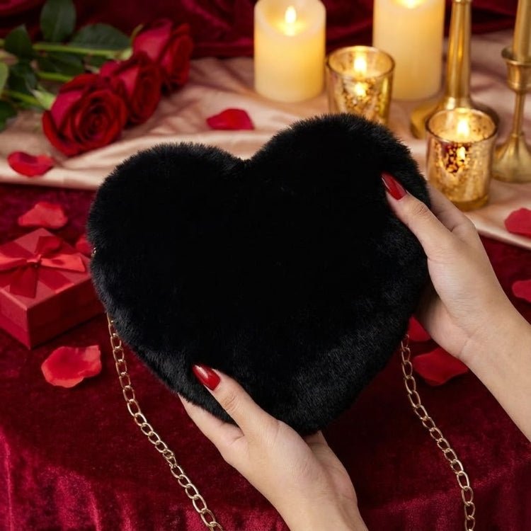 A woman's hands with red nails holding a plush black faux fur heart-shaped bag with a gold chain strap, set against a romantic backdrop with candles and roses.