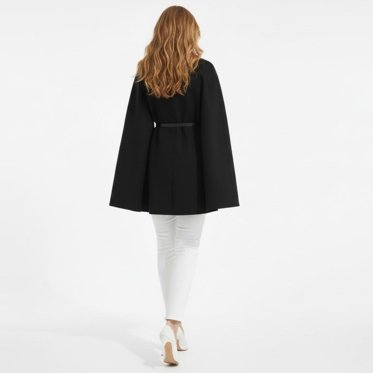 Back view of a woman in the Kouvr Fashion black cape coat, highlighting the clean lines and the slim black belt cinching the waist.