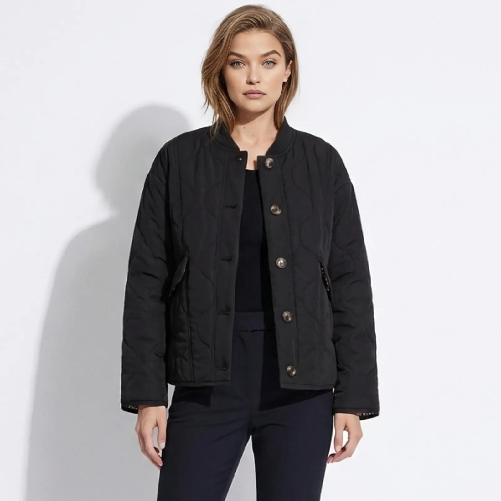Model wearing the Kouvr Fashion black collarless quilted liner jacket with button front, styled with black trousers.