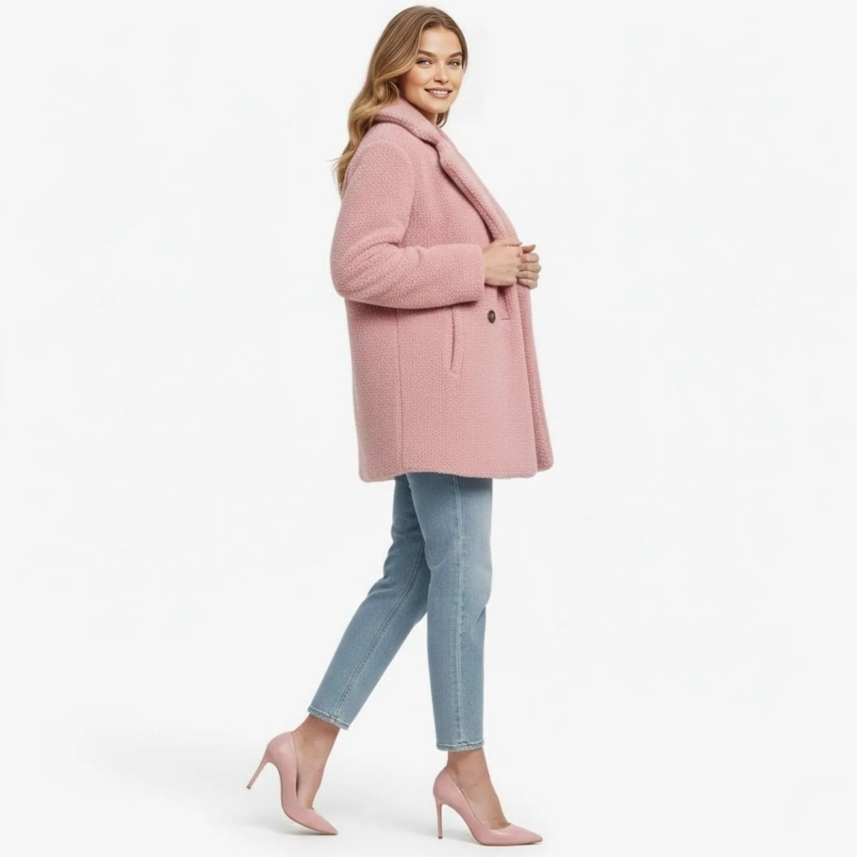 Side profile of a woman walking in a blush pink teddy coat, highlighting its mid-thigh length, fit, and elegant drape over blue jeans.