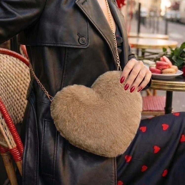 A woman in a black leather trench coat carrying the Kouvr Fashion brown plush faux fur heart-shaped bag with a gold chain strap while sitting at a Parisian cafe.