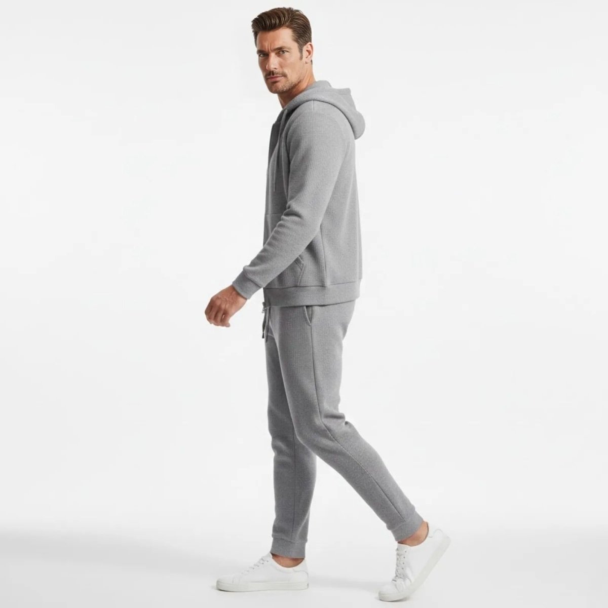 Side profile of a model walking in the grey textured tracksuit set from Kouvr Fashion, showcasing the tailored fit of the hoodie and joggers.