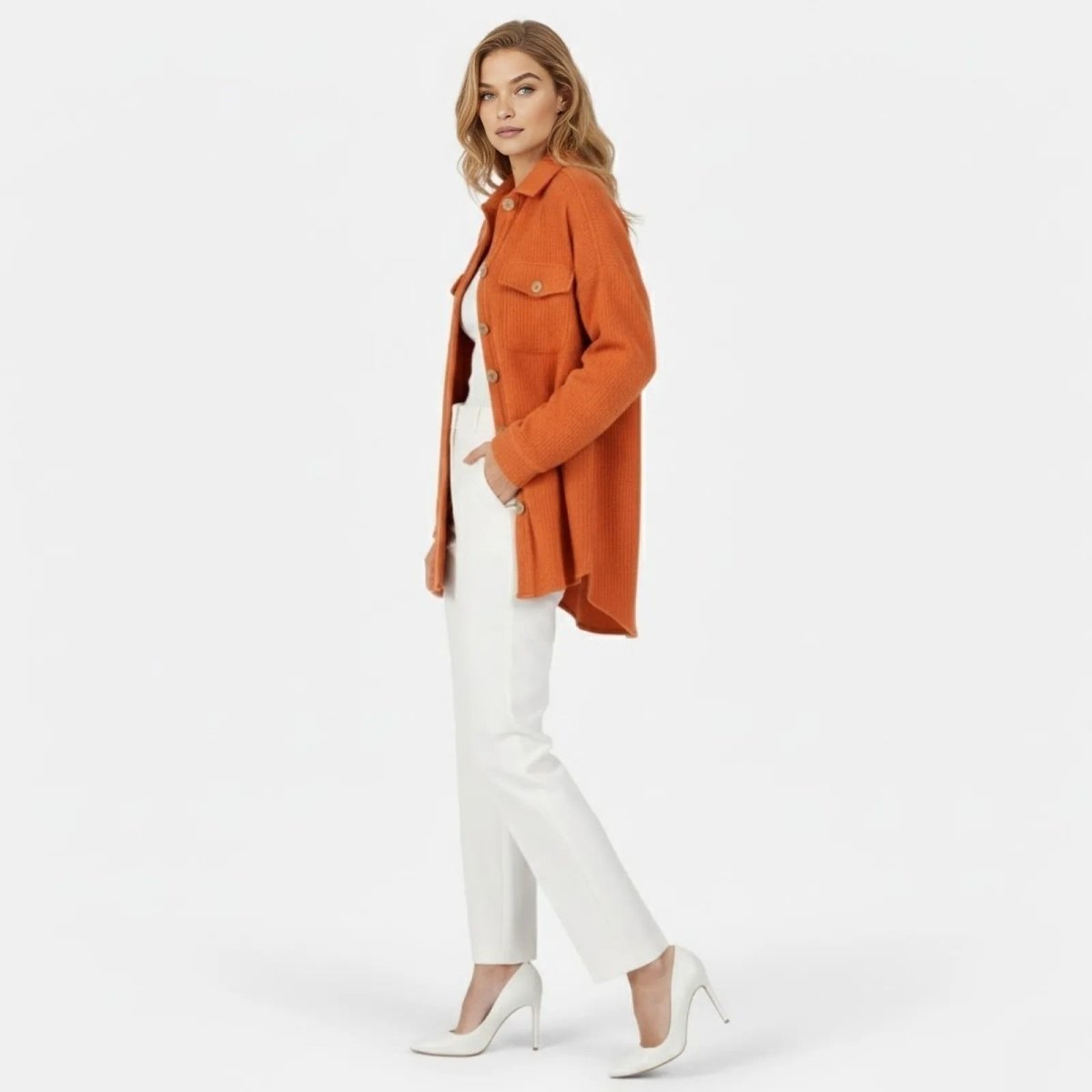 Side profile of a woman wearing the burnt orange oversized waffle knit shacket, showing its length and relaxed drape over white trousers.
