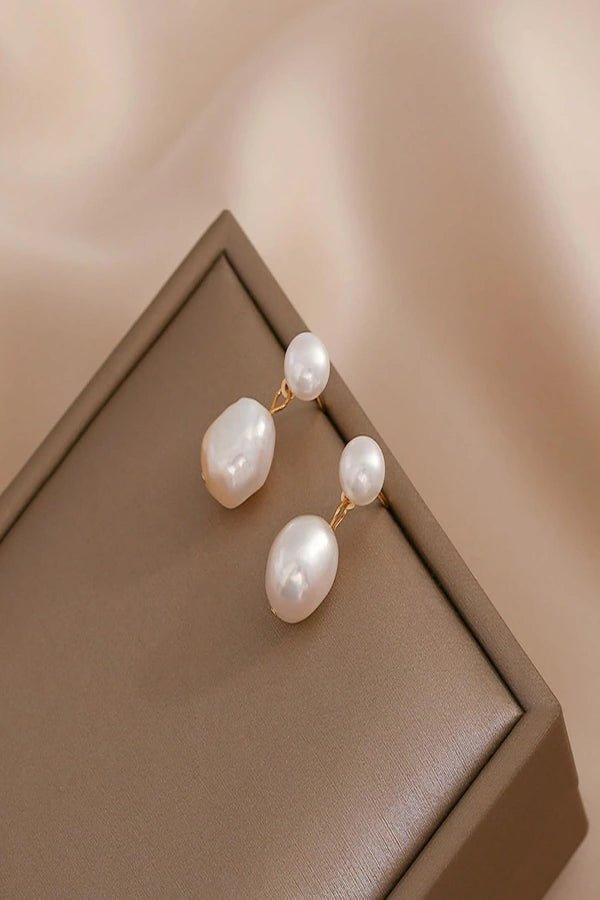 Pearl Kouvr earrings on a brown jewelry box with a soft beige background