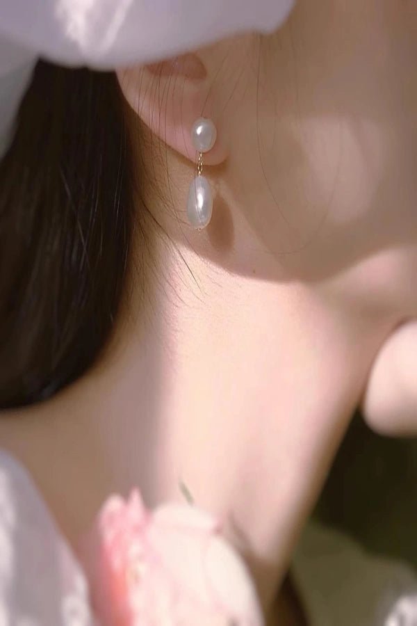 Close-up of a person wearing pearl Kouvr earrings with a soft focus background