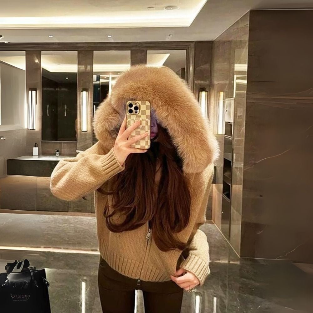 Person wearing a brown kouvr sweater with a fur-lined hood in a modern interior setting.