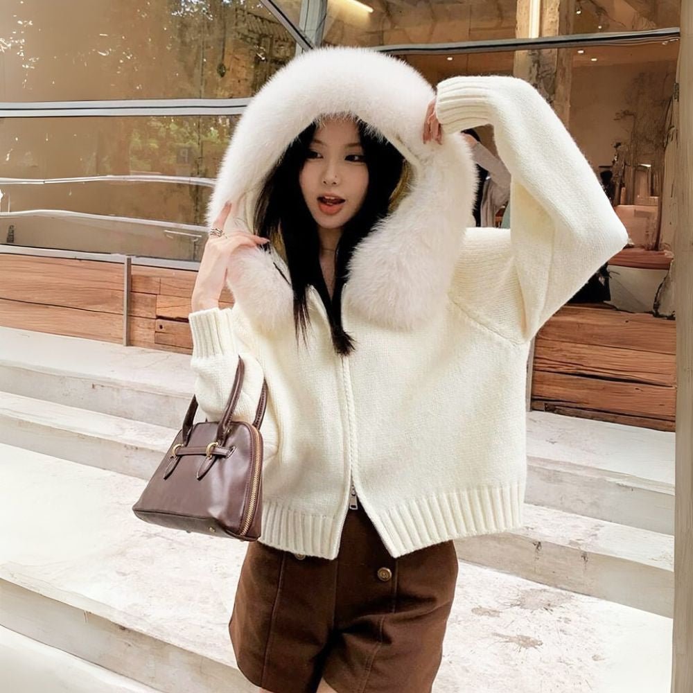 Woman wearing a ivory sweater with a fur-lined hood, holding a brown handbag.