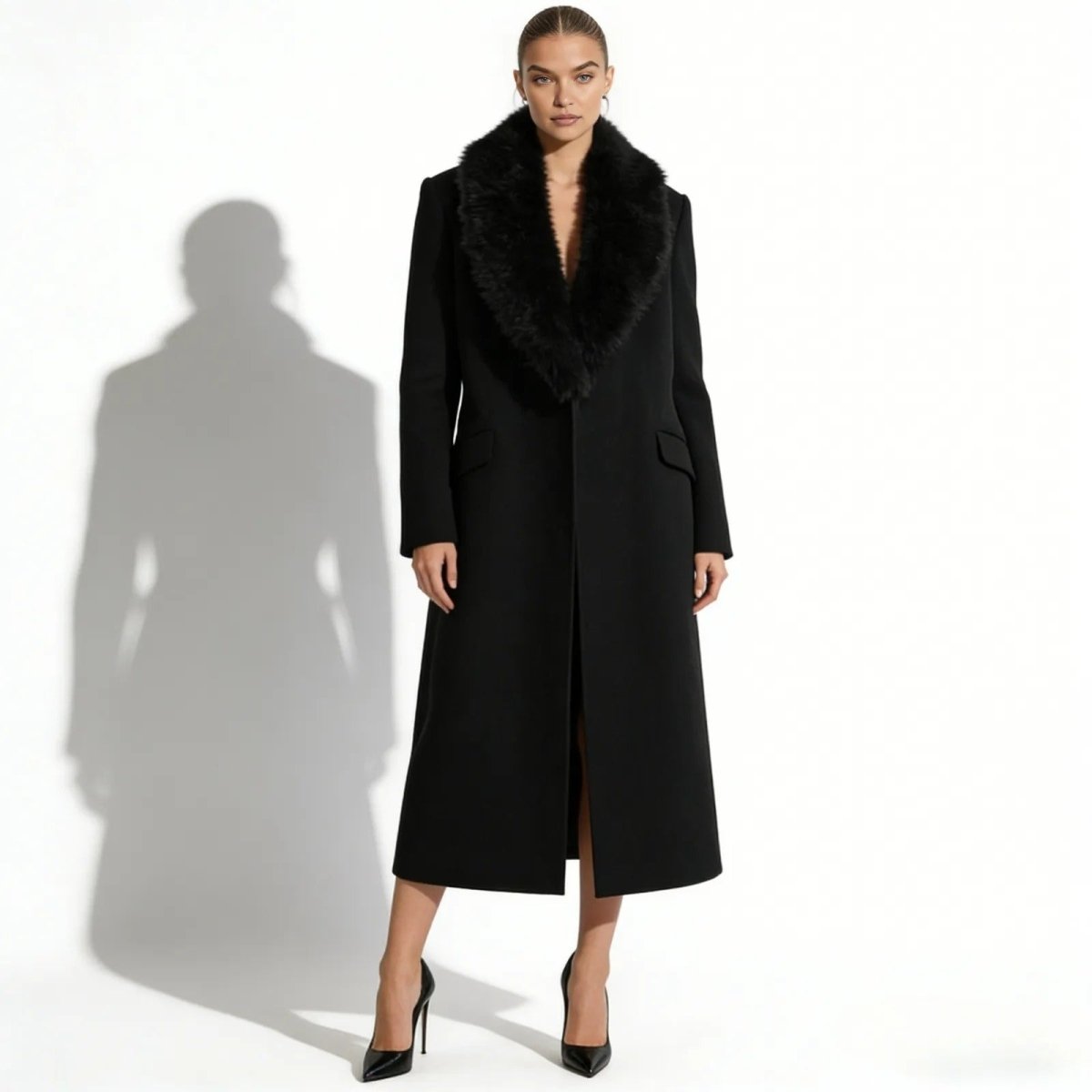 Model facing forward in a Kouvr Fashion long black wool overcoat with a wide faux fur collar, styled open without a belt.