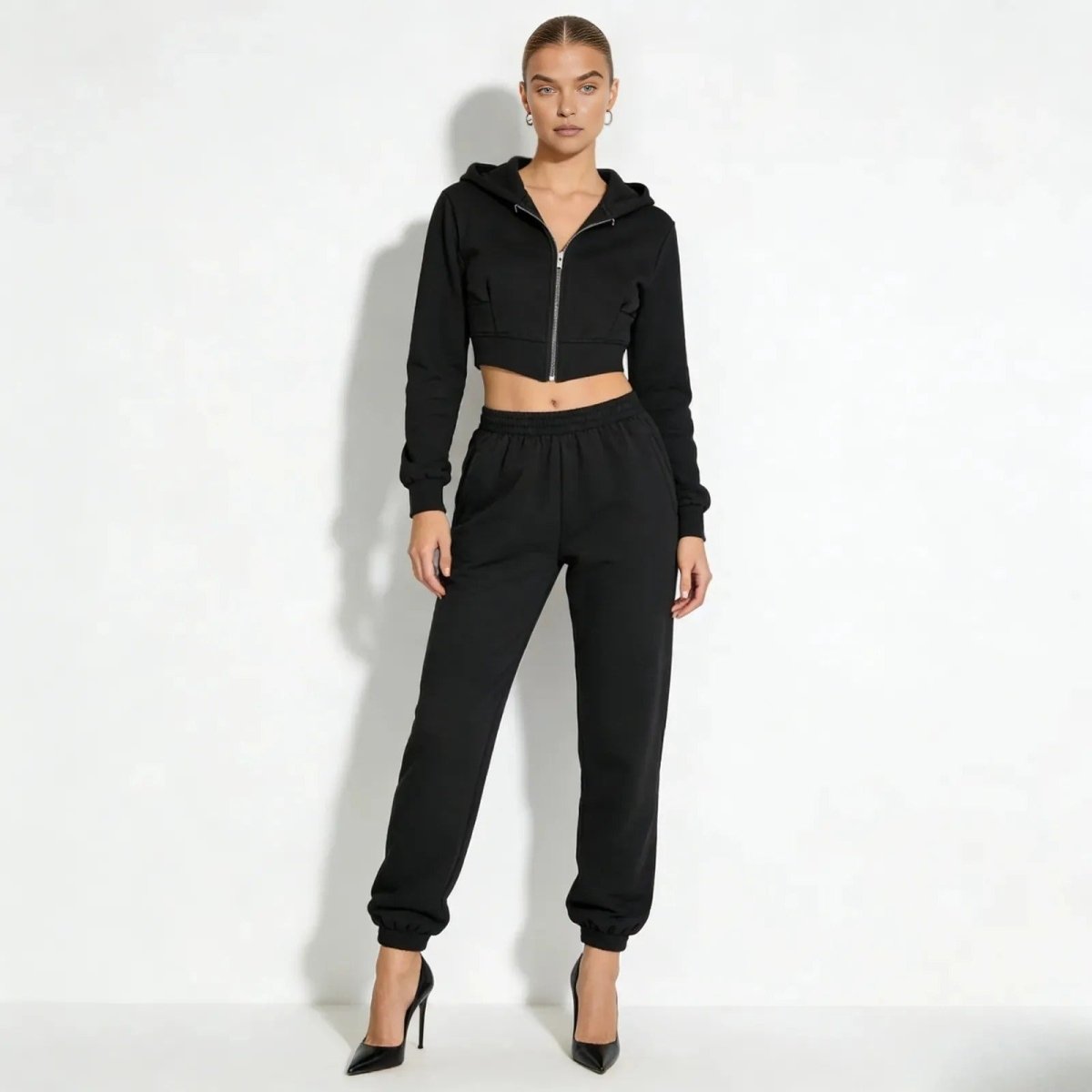 Model wearing the Kouvr Fashion black luxe corset zip hoodie and matching high-waist joggers, full front view with black stilettos.