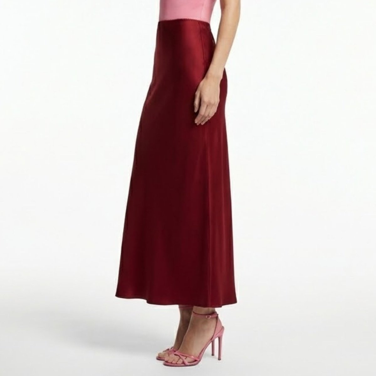 Close-up detail of the liquid satin fabric and fit of the high-waisted Ourania maxi skirt in deep red.
