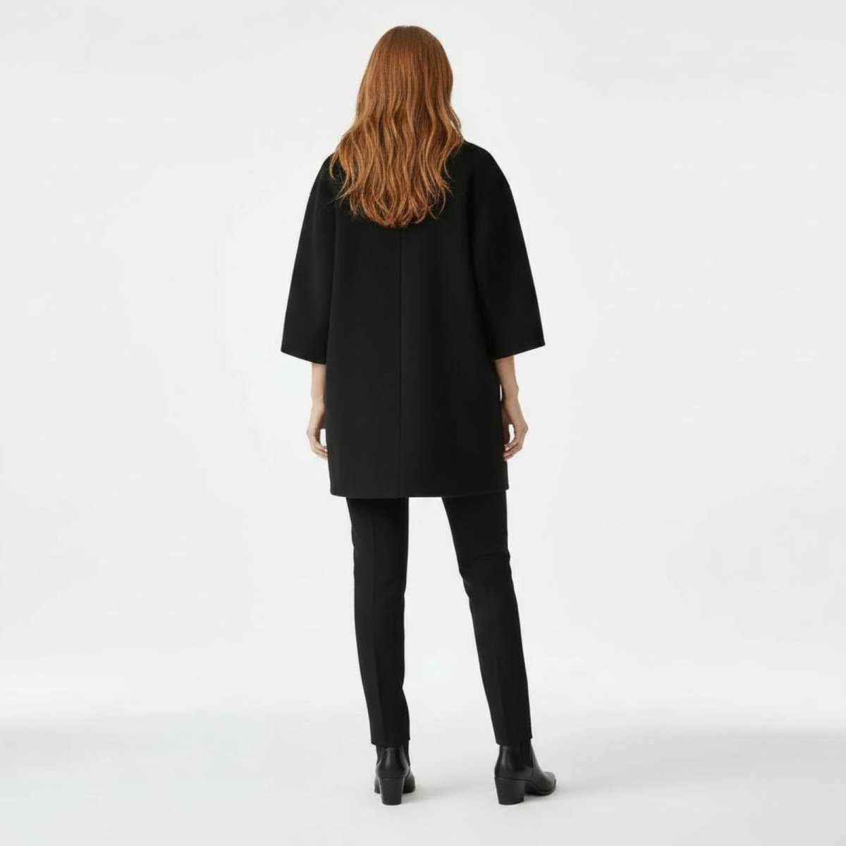 Back view of a model in the Kouvr Fashion minimalist black wool coat, highlighting the center seam and sleeve length.