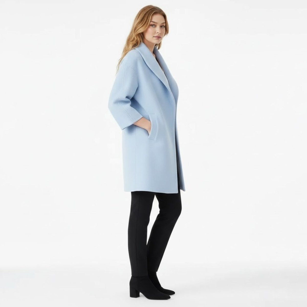 Side profile of a woman in a relaxed-fit sky blue cocoon coat with her hand in the pocket, showing the three-quarter sleeve length.