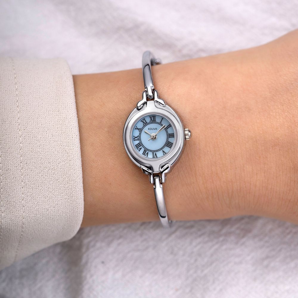 Silver kouvr watch with a blue face on a wrist against a neutral background