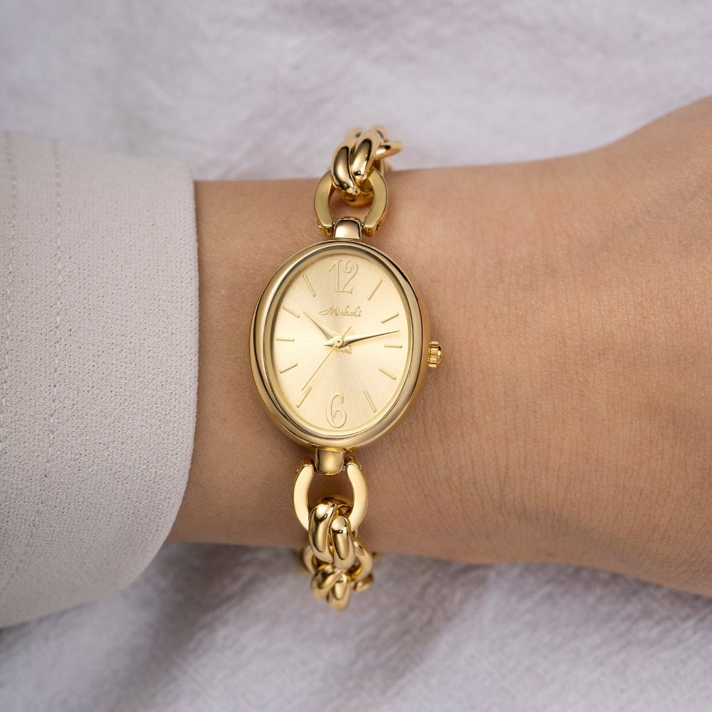 Gold Kouvr wristwatch with chain strap on a wrist against a neutral background
