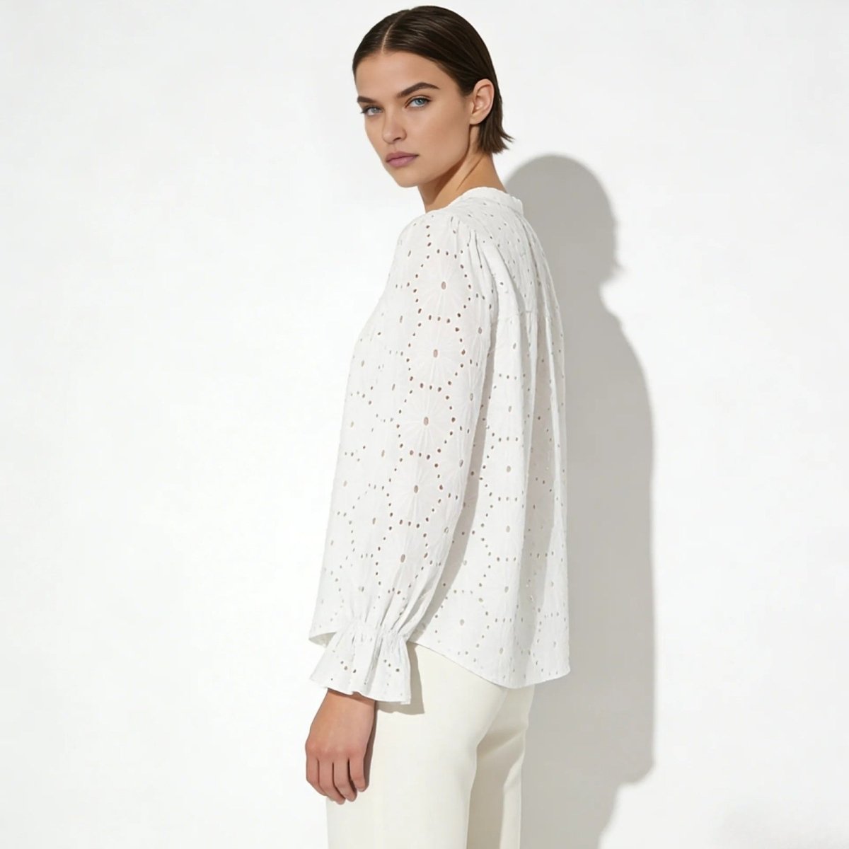 Side view of a model in a white long-sleeve eyelet blouse showing the relaxed fit and ruffled cuff detail.