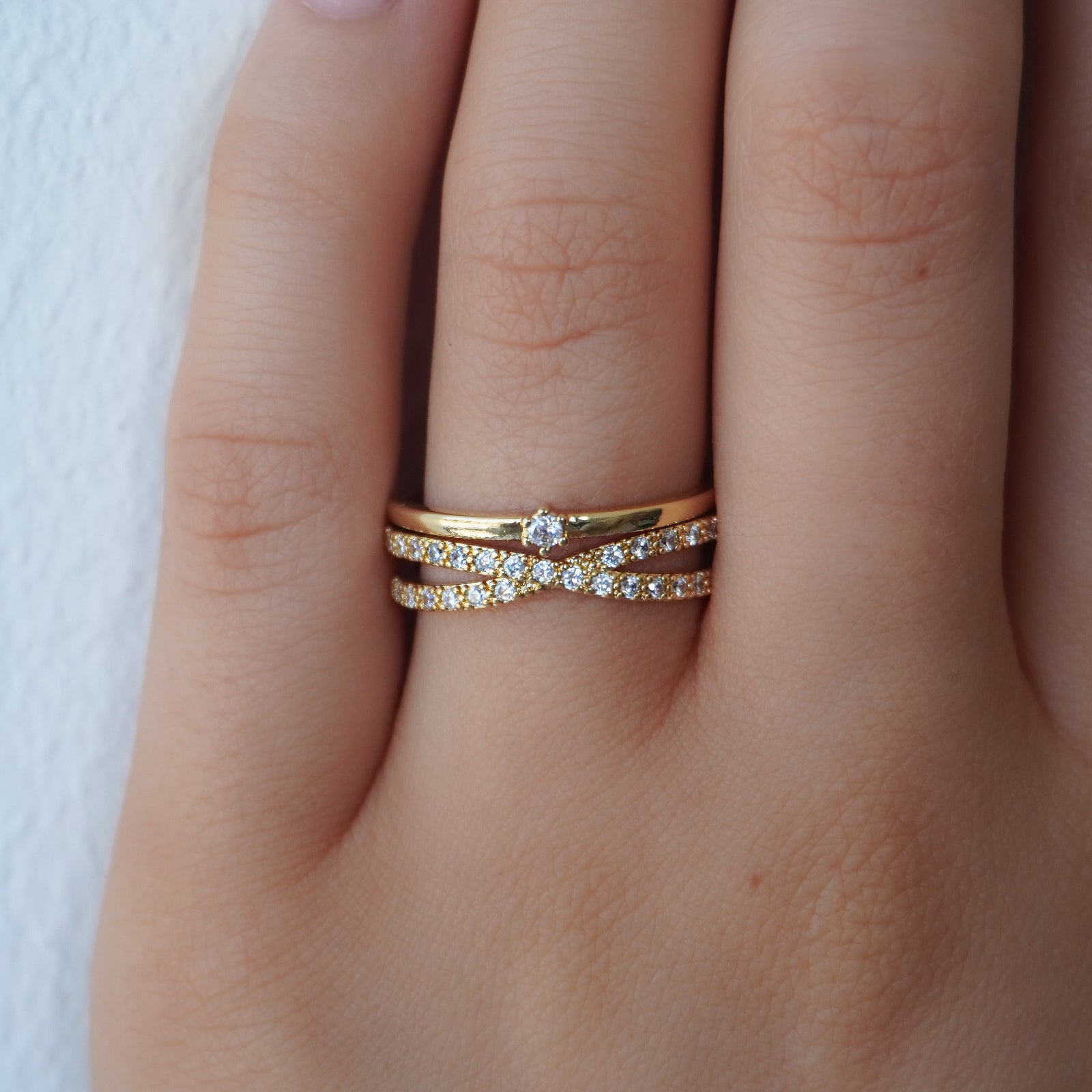 A woman's hand wearing the Kouvr Fenna 18k gold vermeil criss cross pave diamond ring, stacked with a simple gold band.