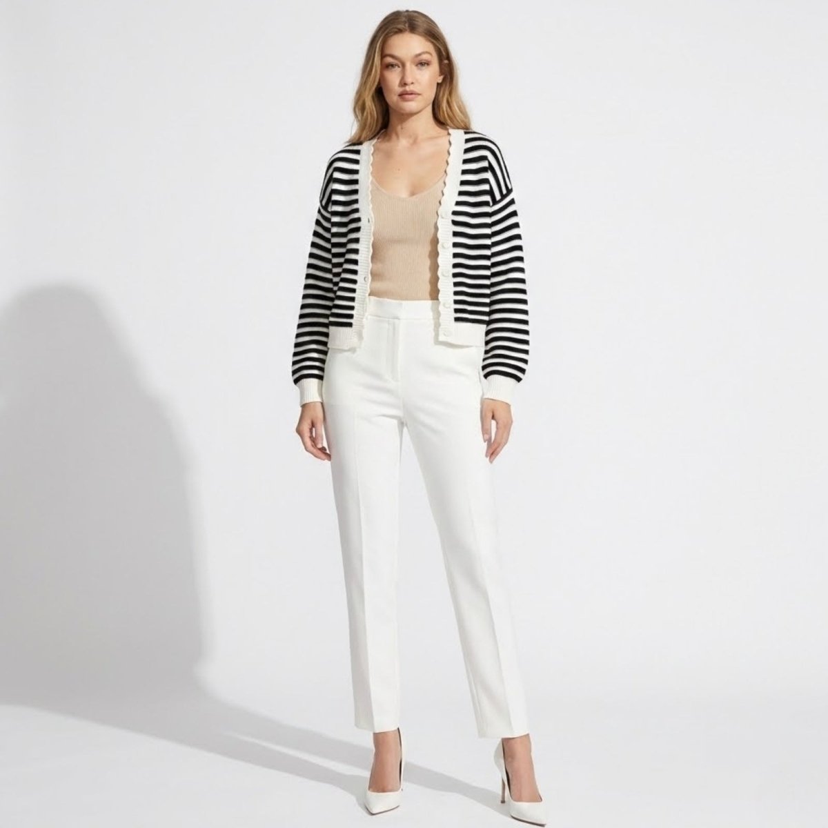 Model wearing the Kouvr black and white Fern stripe cardigan with white trousers, showcasing the v-neck and scallop trim.