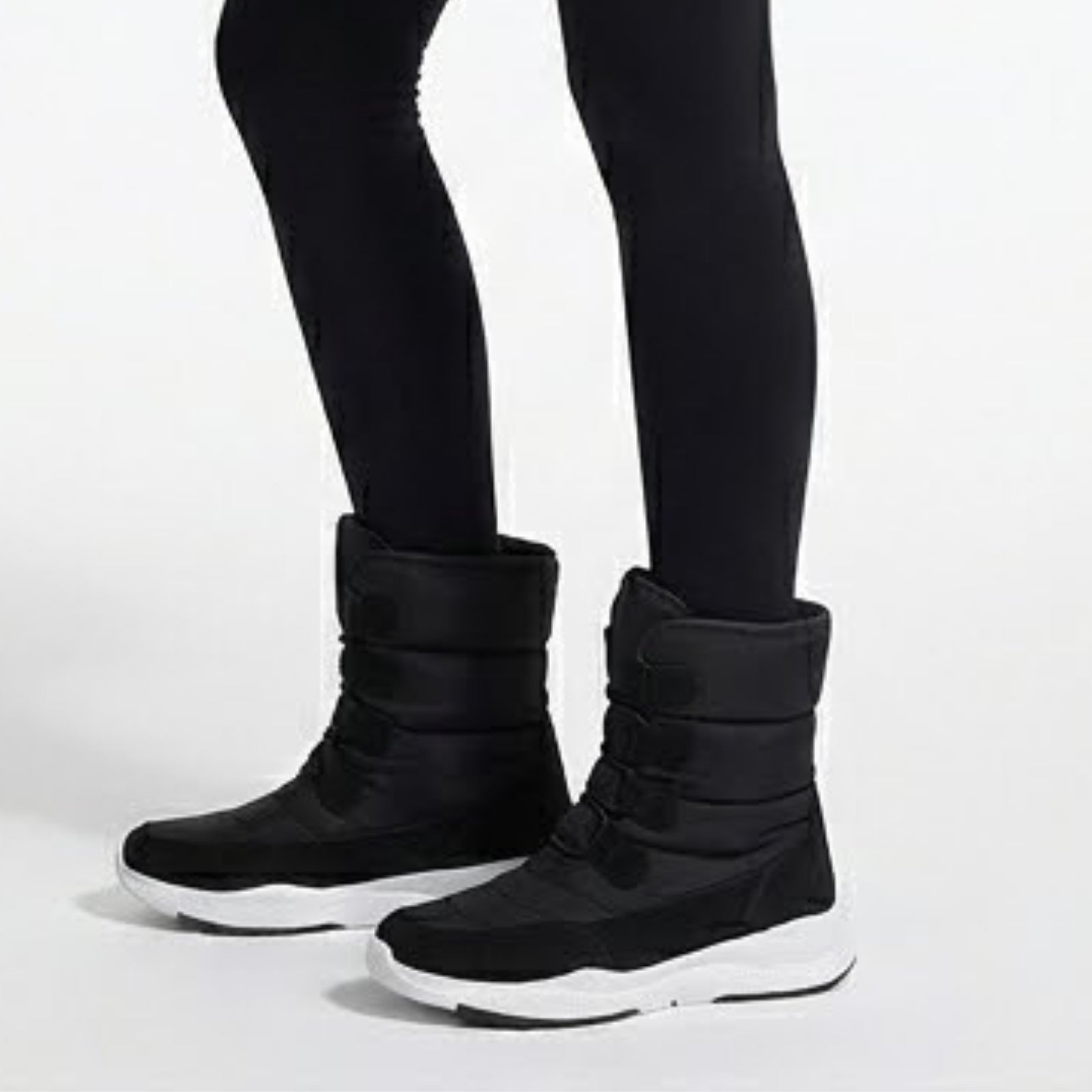 A close-up side view of the Kouvr Gianna black insulated snow boots, showing the adjustable straps and chunky white sneaker sole.